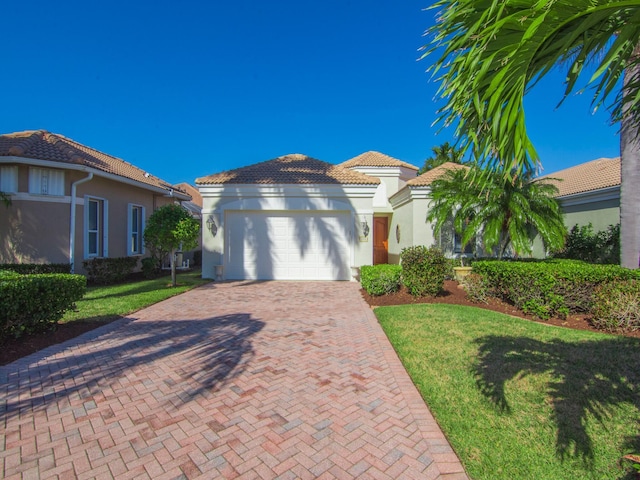 view of front of home with a tiled roof, an attached garage, decorative driveway, a front lawn, and stucco siding