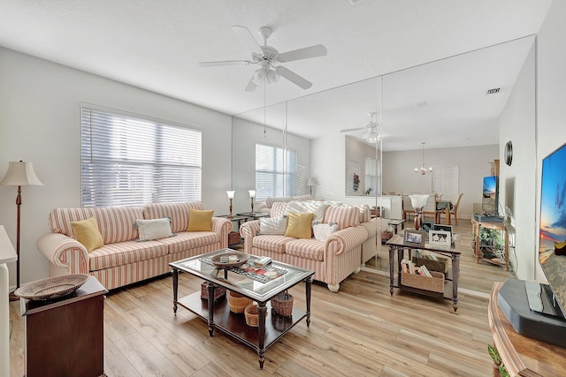 living room with light wood-style floors, visible vents, a textured ceiling, and ceiling fan with notable chandelier