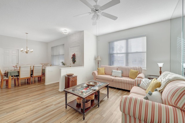 living room featuring ceiling fan with notable chandelier, light hardwood / wood-style floors, and a textured ceiling