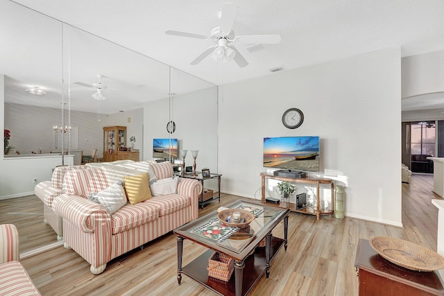 living room with ceiling fan with notable chandelier and light hardwood / wood-style floors