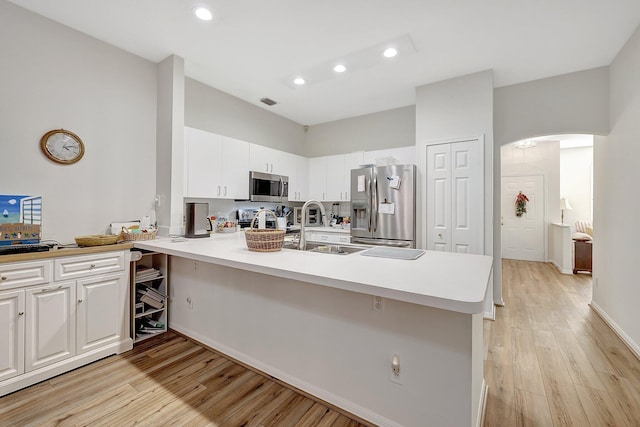 kitchen featuring sink, light hardwood / wood-style flooring, kitchen peninsula, white cabinets, and appliances with stainless steel finishes