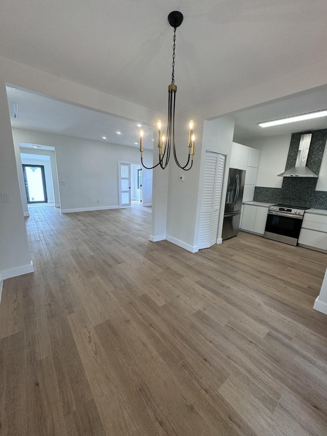 kitchen featuring wall chimney exhaust hood, stainless steel appliances, tasteful backsplash, decorative light fixtures, and white cabinets