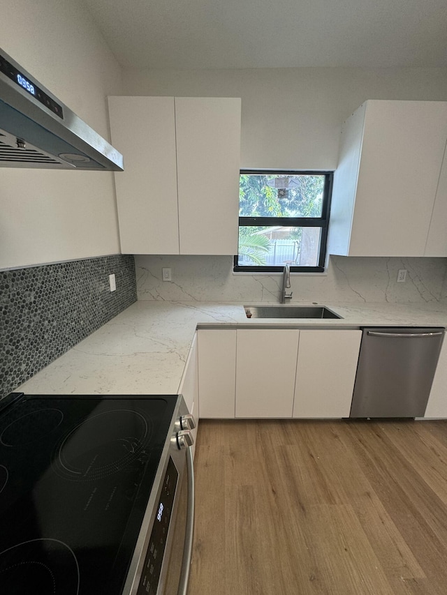 kitchen with light wood-type flooring, stainless steel appliances, wall chimney range hood, sink, and white cabinets