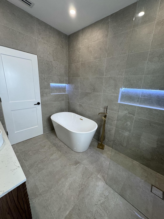 bathroom with a washtub, vanity, and tile walls