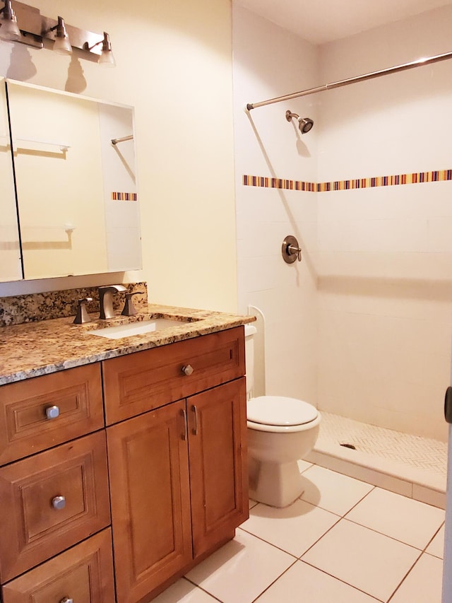 bathroom featuring toilet, tile patterned flooring, vanity, and tiled shower