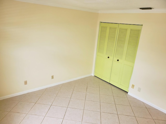 unfurnished bedroom with light tile patterned floors, crown molding, and a closet