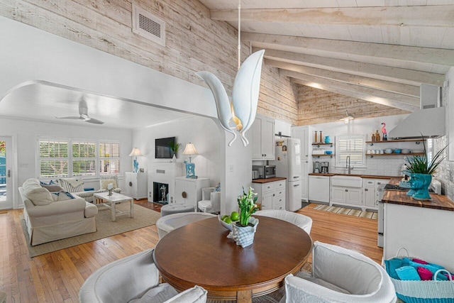 dining room with light wood-type flooring, ceiling fan, sink, beam ceiling, and high vaulted ceiling