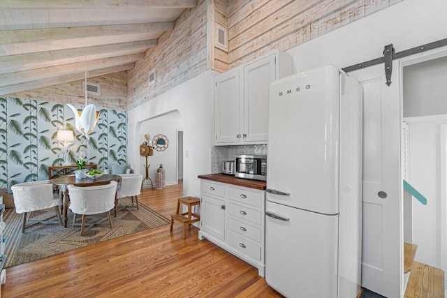 kitchen with high vaulted ceiling, white cabinets, white refrigerator, a barn door, and butcher block countertops