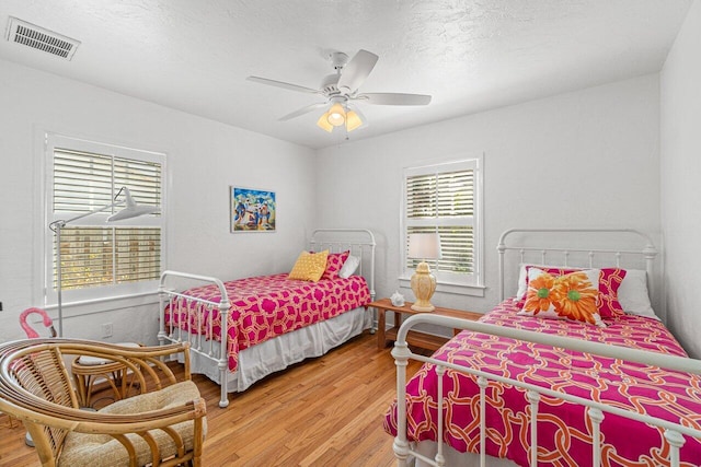 bedroom featuring wood-type flooring, a textured ceiling, multiple windows, and ceiling fan