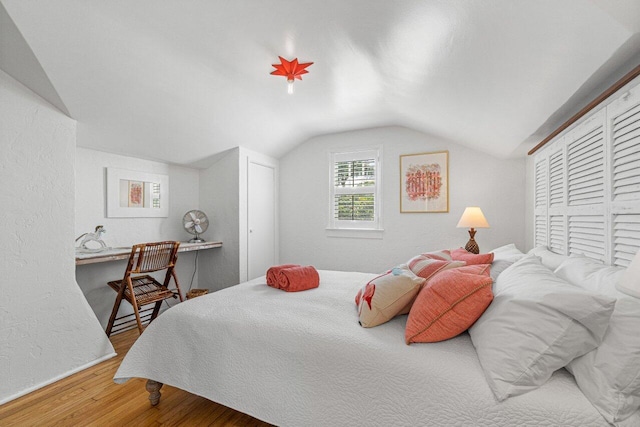 bedroom featuring hardwood / wood-style floors, lofted ceiling, and a closet