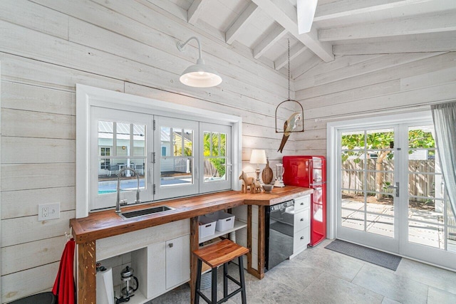 kitchen with wooden counters, wooden walls, pendant lighting, lofted ceiling with beams, and dishwasher