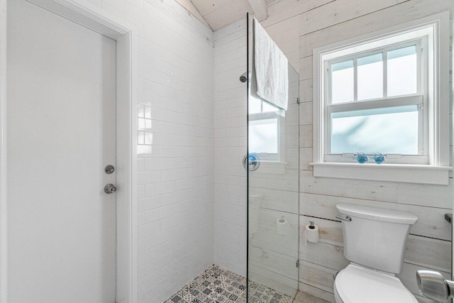 bathroom featuring a tile shower, wooden walls, and toilet