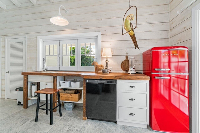 kitchen featuring dishwasher, sink, butcher block countertops, wood walls, and white cabinets