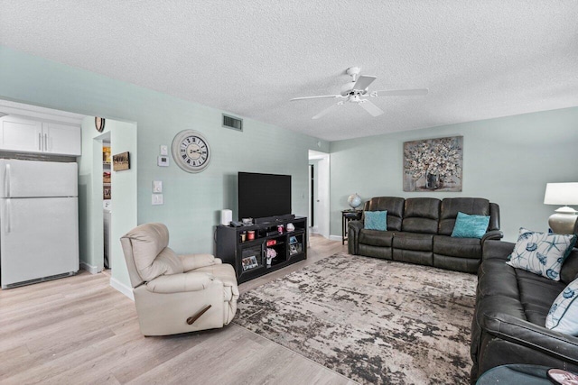 living room with ceiling fan, light wood-type flooring, and a textured ceiling