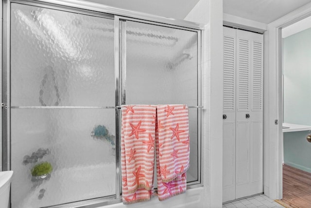 bathroom with wood-type flooring and bath / shower combo with glass door