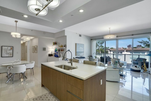 kitchen with sink, light tile patterned floors, an island with sink, decorative light fixtures, and a water view