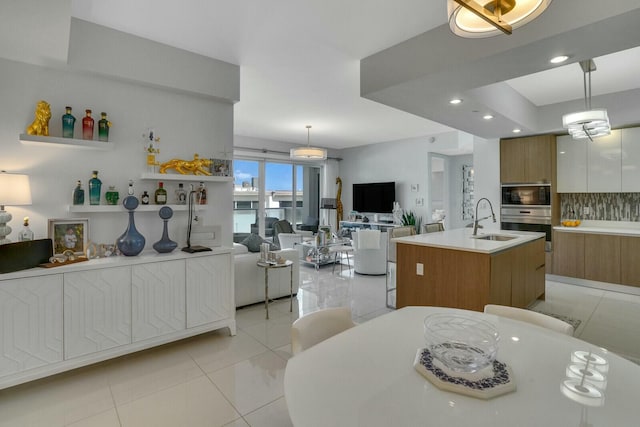 kitchen featuring light tile patterned flooring, pendant lighting, a center island with sink, and sink