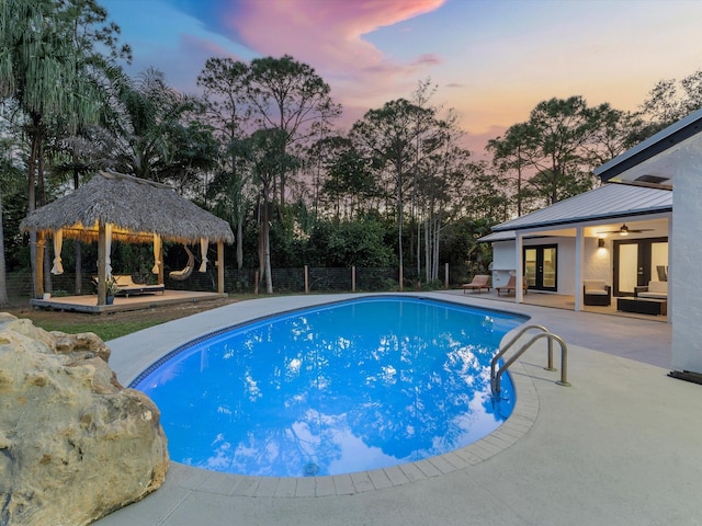 pool at dusk featuring a gazebo, an outdoor hangout area, a patio, and french doors