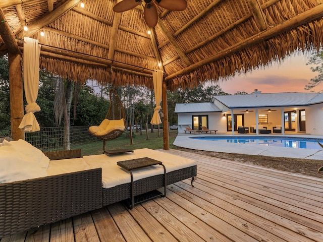 pool at dusk with a gazebo, outdoor lounge area, ceiling fan, and a deck