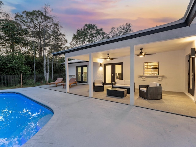 pool at dusk featuring a patio, an outdoor hangout area, ceiling fan, and french doors