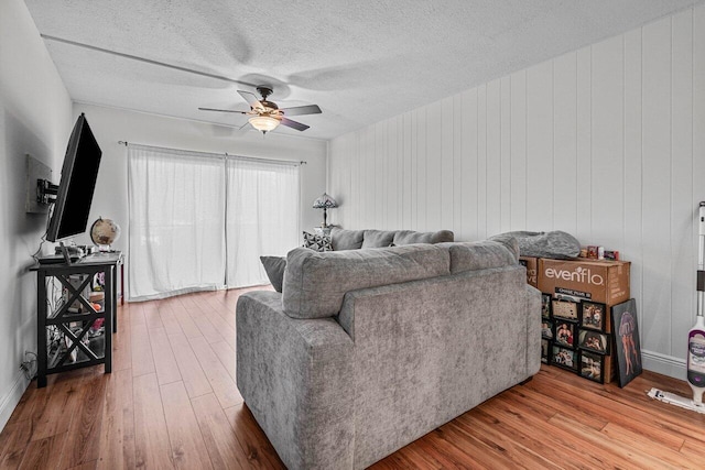 living room featuring ceiling fan, wooden walls, wood-type flooring, and a textured ceiling