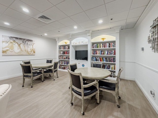 dining area featuring a paneled ceiling, built in shelves, ornamental molding, and light wood-type flooring