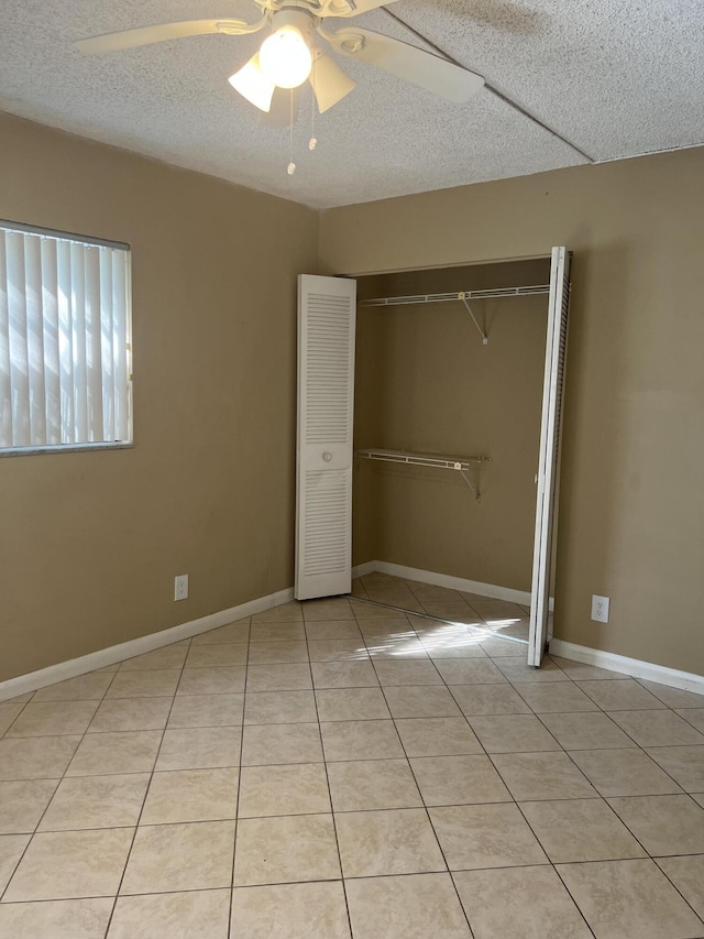 unfurnished bedroom with ceiling fan, a closet, light tile patterned flooring, and a textured ceiling