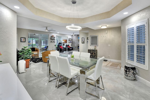 dining room with ceiling fan with notable chandelier and a raised ceiling