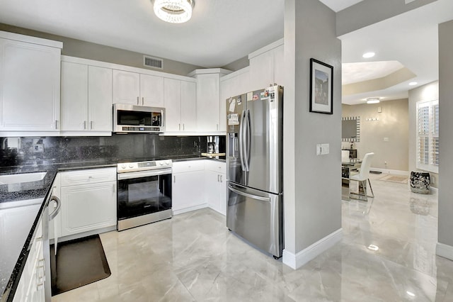 kitchen with tasteful backsplash, dark stone counters, stainless steel appliances, sink, and white cabinetry