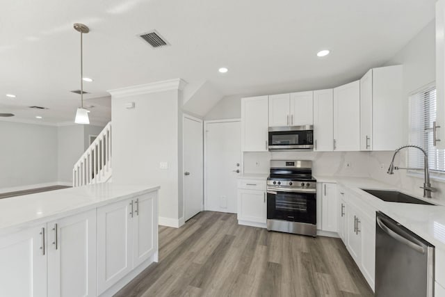 kitchen with sink, light hardwood / wood-style flooring, appliances with stainless steel finishes, decorative light fixtures, and white cabinetry