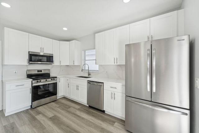 kitchen with sink, stainless steel appliances, light hardwood / wood-style floors, decorative backsplash, and white cabinets