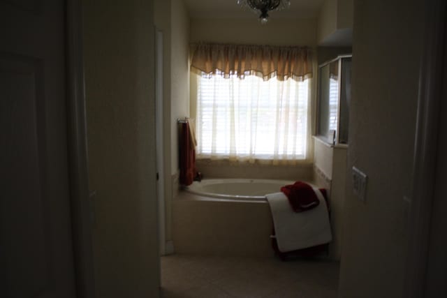 bathroom featuring tile patterned flooring, a bath, and a chandelier