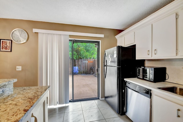 kitchen with black appliances, white cabinets, light tile patterned floors, and a textured ceiling