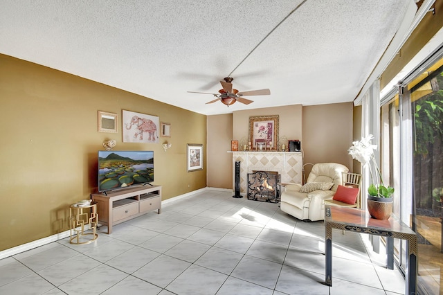 sitting room with a tiled fireplace, ceiling fan, light tile patterned floors, and a textured ceiling