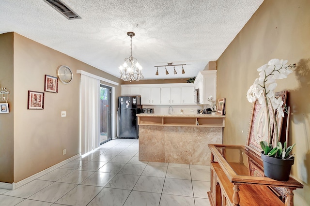 kitchen featuring kitchen peninsula, black fridge, a textured ceiling, decorative light fixtures, and white cabinetry