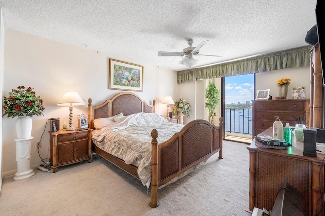 carpeted bedroom featuring ceiling fan, access to exterior, a textured ceiling, and a water view