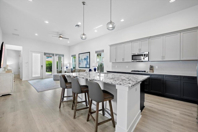 kitchen featuring stainless steel appliances, a kitchen island with sink, ceiling fan, decorative light fixtures, and light hardwood / wood-style flooring