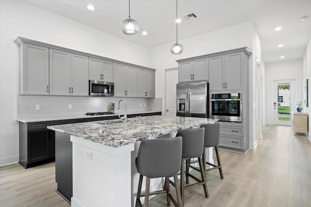 kitchen featuring appliances with stainless steel finishes, sink, light hardwood / wood-style flooring, gray cabinets, and an island with sink