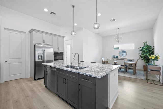 kitchen with stainless steel appliances, sink, light hardwood / wood-style flooring, gray cabinets, and an island with sink