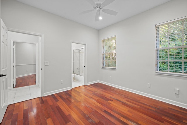 unfurnished bedroom with ensuite bathroom, ceiling fan, hardwood / wood-style flooring, a spacious closet, and a closet