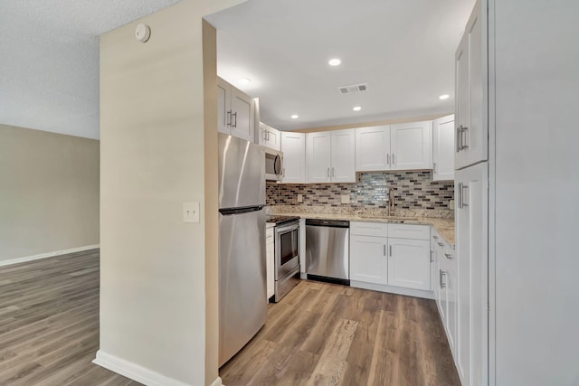 kitchen with stainless steel appliances, tasteful backsplash, light stone counters, light hardwood / wood-style flooring, and white cabinets