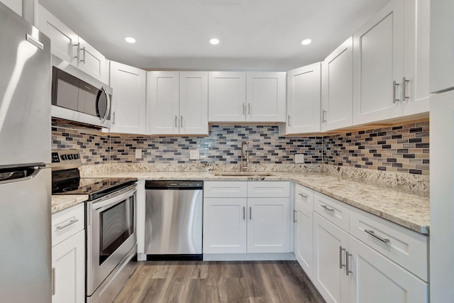 kitchen featuring decorative backsplash, appliances with stainless steel finishes, sink, hardwood / wood-style flooring, and white cabinetry