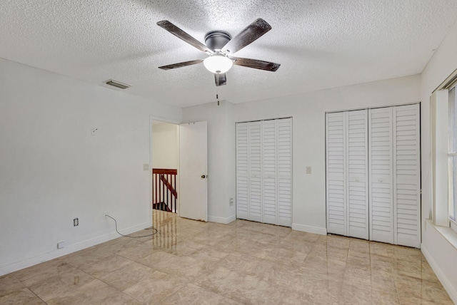 unfurnished bedroom with a textured ceiling, two closets, and ceiling fan