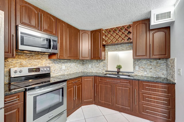 kitchen with appliances with stainless steel finishes, dark stone counters, and sink