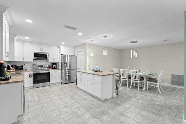 kitchen with white cabinets, decorative light fixtures, a center island, and stainless steel appliances