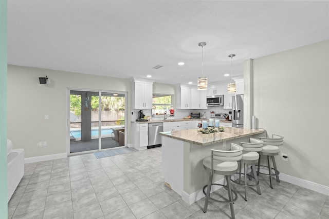 kitchen featuring white cabinets, sink, decorative light fixtures, light stone counters, and stainless steel appliances