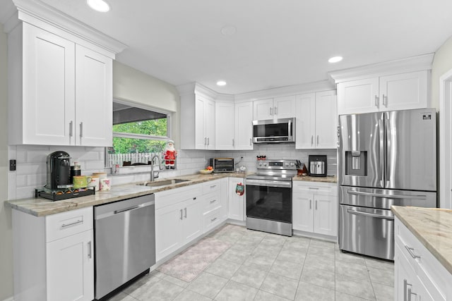 kitchen with tasteful backsplash, light stone counters, stainless steel appliances, sink, and white cabinetry