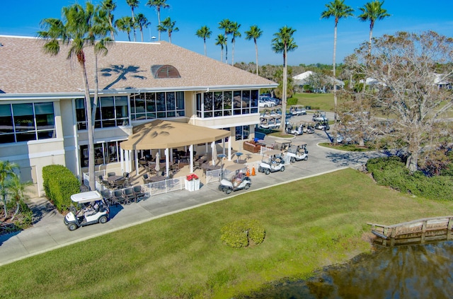 back of property featuring a water view, a sunroom, a patio area, and a lawn