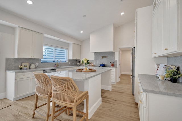 kitchen featuring white cabinets, sink, light wood-type flooring, a kitchen island, and a kitchen bar