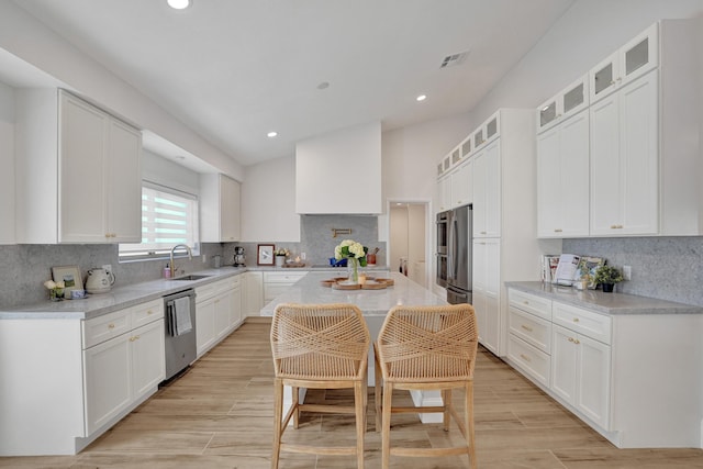 kitchen with white cabinetry, sink, stainless steel appliances, vaulted ceiling, and a kitchen island